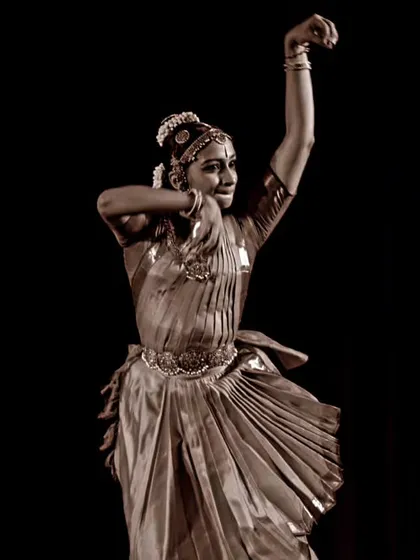A sepia-toned shot capturing the timeless quality of Indian classical dance. This dynamic pose is from a pure dance sequence, showcasing the sculpture-like beauty of Bharatanatyam.