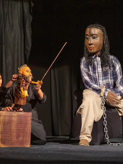 A giant, masked puppet representing Gulliver interacts with a smaller rod puppet of a Lilliputian king. Our production of 'Gulliver's Travel' uses a dramatic difference in scale to tell the classic story.