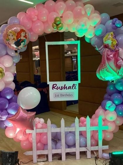 A princess-themed first birthday photo booth. The circular balloon arch includes a cutout frame and character foil balloons.