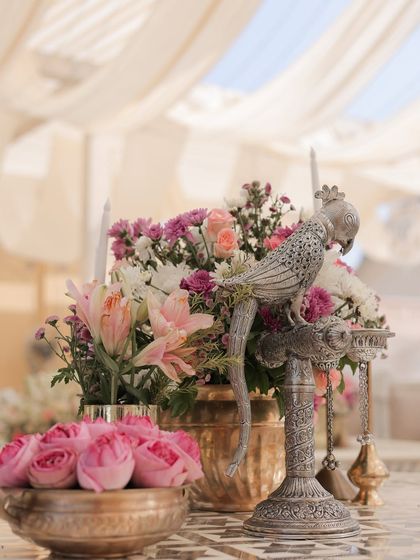 A bowl of fresh pink roses and a silver parrot prop create a beautiful focal point on this mirror-work table. Fresh flowers are always the heart of my designs.