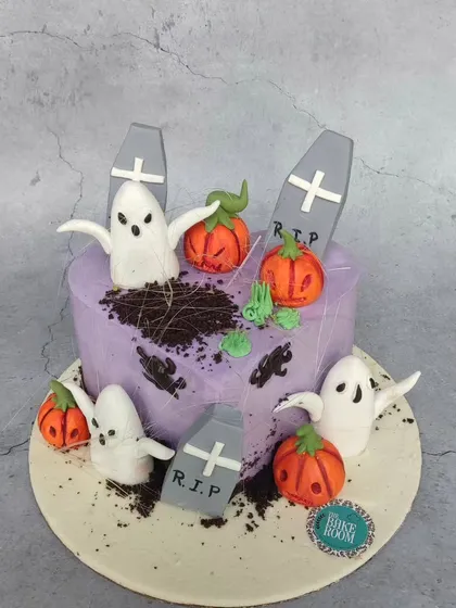 A spooky and fun Halloween cake featuring a graveyard scene. It has edible ghosts, pumpkins, and tombstones, with cookie crumble 'dirt' for a realistic effect.
