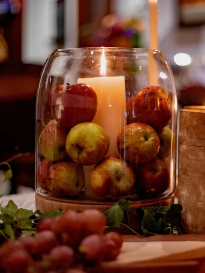 A focused shot on the apple-filled hurricane, with fresh grapes in the foreground. This composition emphasizes the use of fresh, natural produce as a key component of the decor.