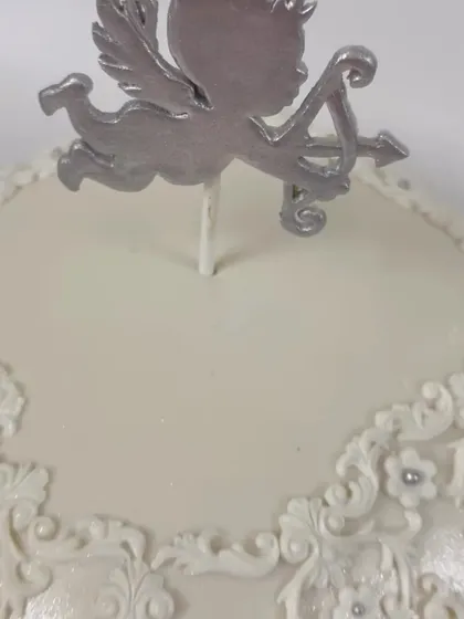 A close-up of the silver cupid topper and the delicate, hand-piped lace detail on the angel-themed cake. This level of detail adds a touch of vintage elegance to the design.