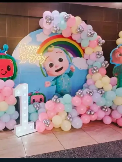 A pastel Cocomelon theme for a first birthday. This gentle color palette offers a softer take on the popular theme, complete with a rainbow, character cutouts, and a light-up number '1'.