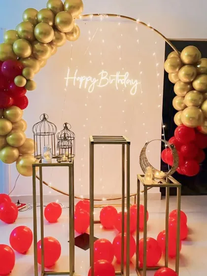 I create simple and elegant decorations for adult birthdays or anniversaries. This setup uses a classic red and gold color scheme with a balloon arch, a neon sign, and minimalist pedestals for a sophisticated look.