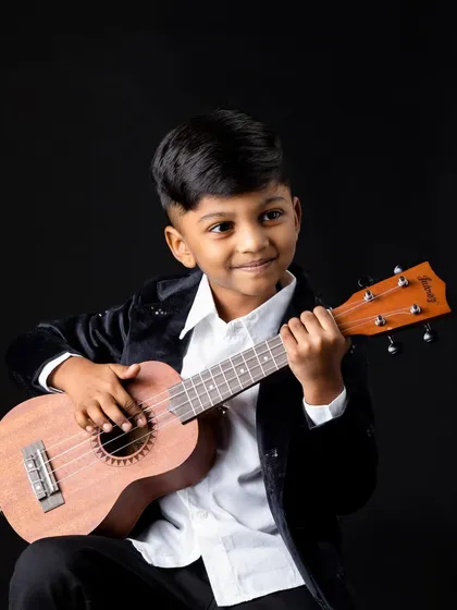 A 5-year-old boy looking like a young musician, strumming a ukulele for his studio portrait.