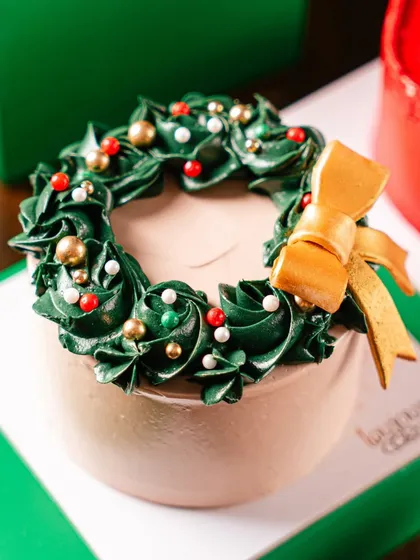 Our Wreath Mini Cake, a small but elegant dessert perfect for individual gifting. The chocolate cake is topped with a beautifully piped green buttercream wreath and a gold bow.