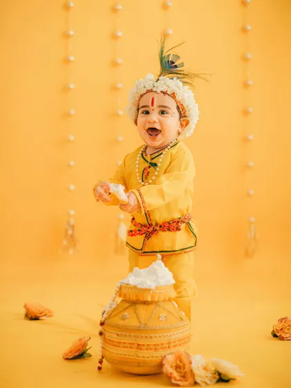A classic studio portrait for Janmashtami. The bright yellow dhoti, peacock feather crown, and a happy, messy face make for an unforgettable photo.