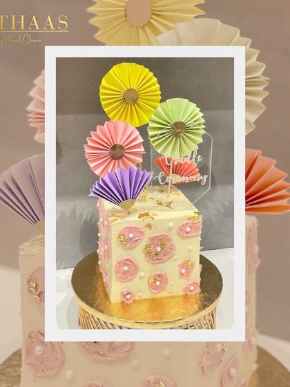 A whimsical and colorful cake perfect for a naming ceremony. The square tier is decorated with painted pink flowers and topped with a vibrant array of paper fans.