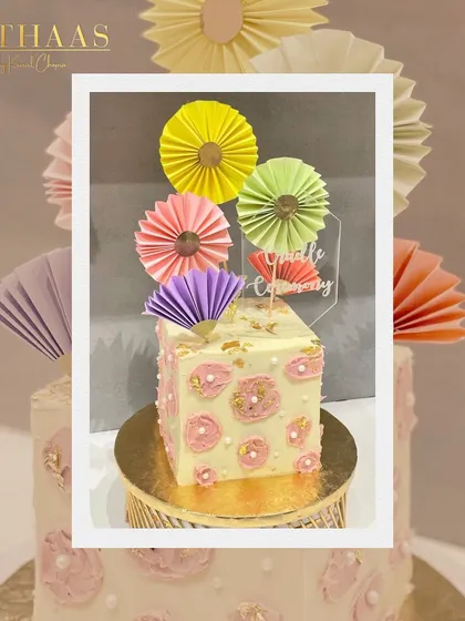 A vibrant and joyful cake for a naming ceremony. This design features colorful paper fans and a soft pink floral pattern, creating a festive and celebratory centerpiece.