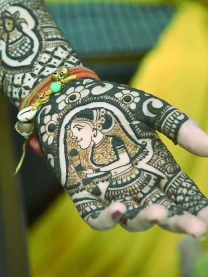 A close-up of the bride's hand, showcasing the beautiful portrait of a bride in her doli, intricately drawn in henna.