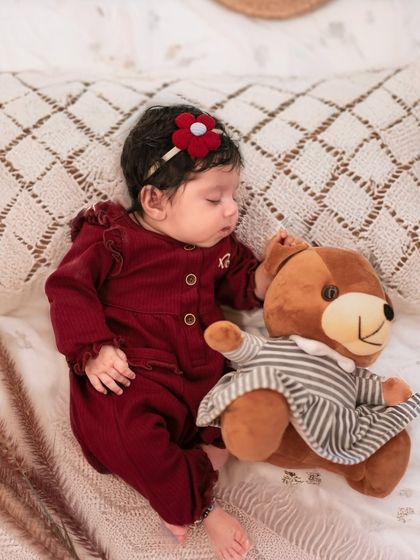 Even while sleeping, the bond is there. A two-month-old baby snuggles with a teddy bear during her cozy Christmas-themed milestone session.