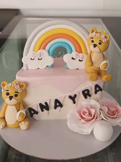 A beautiful cake featuring two teddy bears, a rainbow, and fondant roses. The soft pastel colors make this a perfect choice for a baby shower or first birthday.