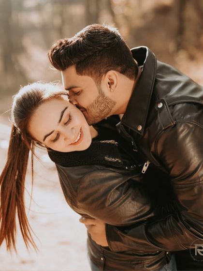 A sweet and spontaneous moment as he kisses her forehead, both of them bundled in leather jackets, capturing the warmth of their affection in a cool outdoor setting.
