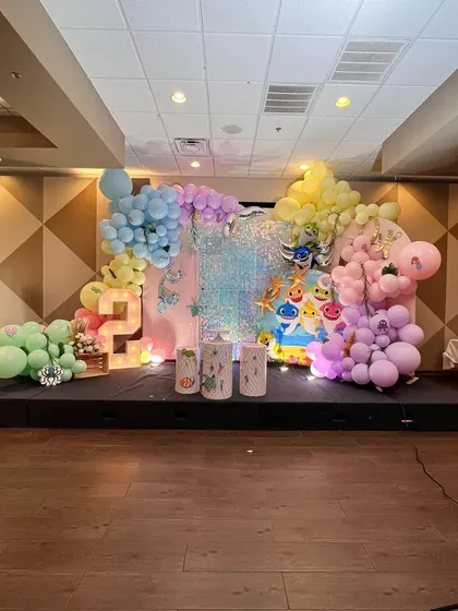 A large-scale Baby Shark stage decoration with pastel-colored organic balloon garlands and a shimmer wall.