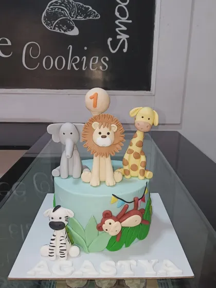 A delightful jungle safari cake for a first birthday. This design includes a lion, elephant, giraffe, zebra, and monkey, all handcrafted from fondant.