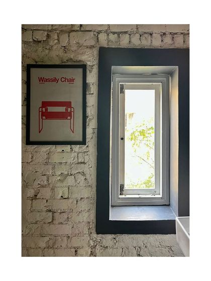 A detail showing the restored whitewashed brick wall and a new window in the co-living apartment. The project involved resurrecting a dilapidated 1960s building, carefully blending old textures with new, modern insertions.