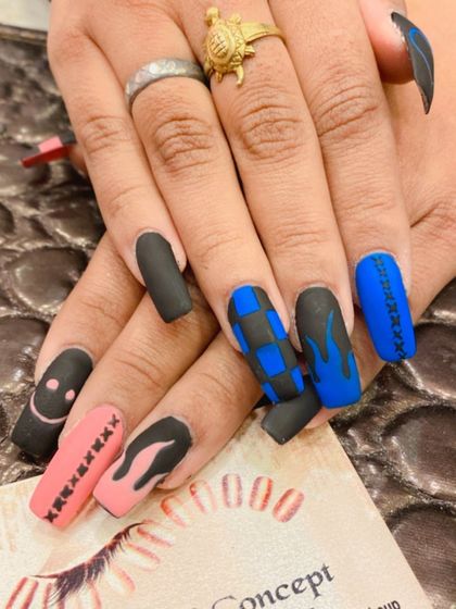 An edgy and eclectic set of long, matte nails. The design includes a mix of black, pink, and blue nails with hand-painted details like smiley faces, checkerboard patterns, and flame art.