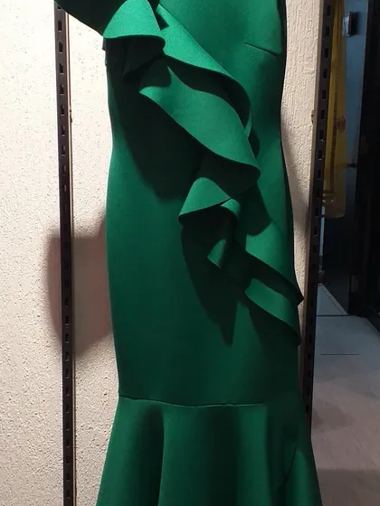 A bold emerald green gown with dramatic cascading ruffles along one side. This sculptural, fashion-forward piece is perfect for someone looking to stand out at a gala or reception.