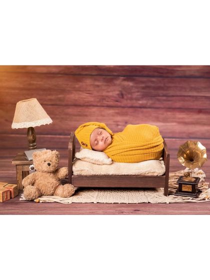A classic newborn setup featuring a baby sleeping on a miniature bed. The scene is completed with a tiny lamp, teddy bear, and gramophone, giving it a vintage and timeless feel.