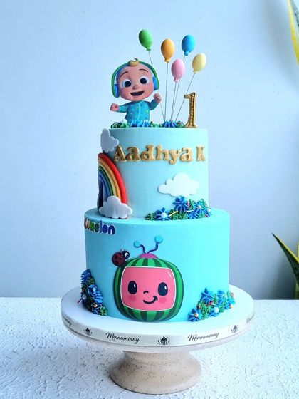 A full view of the two-tier Cocomelon cake on its stand.