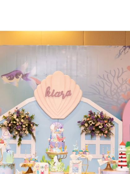 The main backdrop for Kiara's party featured a shell-shaped sign with her name, surrounded by beautiful floral arrangements.