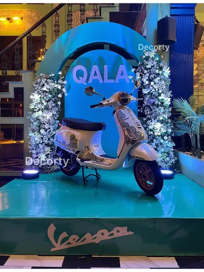 A full shot of the custom painted Vespa on its display stage. The lighting and floral decor work together to create a truly premium and photo-worthy brand moment.