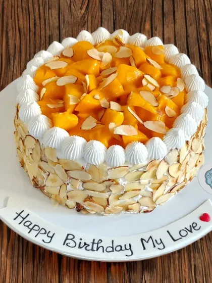 A fresh mango cake with the sides covered in toasted almonds. The combination of sweet mango, light cream, and crunchy nuts is a perfect treat.
