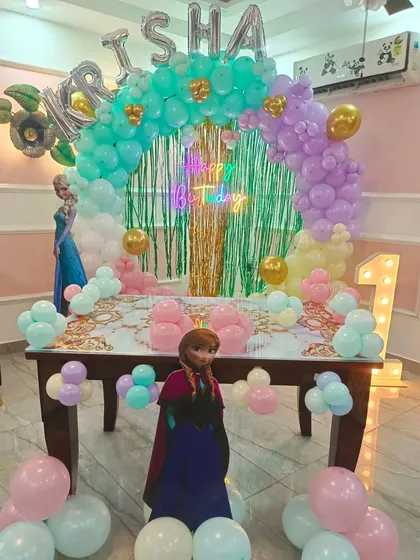 Another take on a Frozen theme for a first birthday. This setup features a pastel balloon arch, a green shimmer backdrop, and cutouts of both Anna and Elsa.