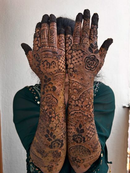 A playful pose showing off the full extent of this bridal mehendi. The design covers both hands and arms with dense, traditional patterns, perfect for wedding photos.