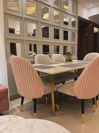 A detailed shot of a dining area with pink channel-tufted chairs and a marble-top table with gold-finished legs. The mirrored wall in the background enhances the sense of space and luxury.