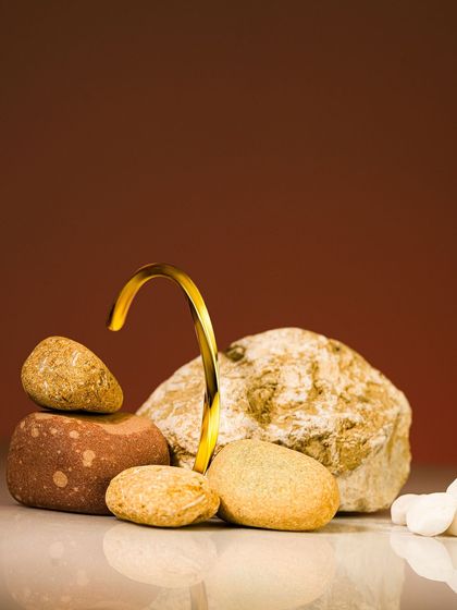 A piece of abstract gold jewelry elegantly placed among natural stones, creating a beautiful contrast between organic and man-made forms.