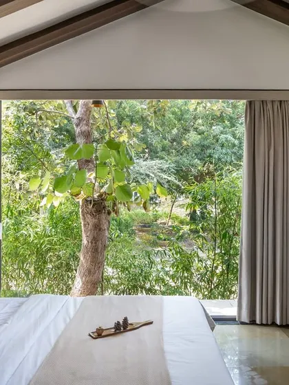 In the Midas Resort, we designed the villa suites to seamlessly merge with the surrounding landscape. This bedroom features a full-height window that opens up to lush greenery, making nature the primary focal point. The interior palette of earthy tones and soft textures creates a tranquil retreat.