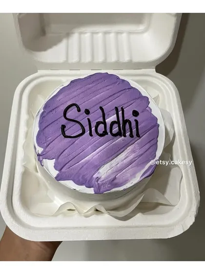 A simple and modern bento cake with a purple brushstroke design and the name 'Siddhi' written across it.