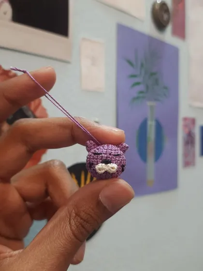 A close-up of a tiny purple cat phone charm. The micro-crochet technique allows for a lot of detail in a very small space.