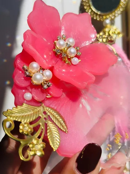 A close up shot showing the detail on a floral Milni plate. You can see the layers of resin, the delicate pearls set in the flower's center, and the intricate golden metal charms.