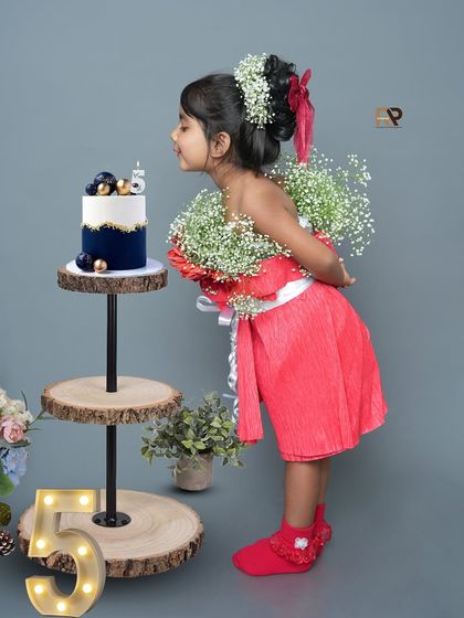 A girl blows out the candle on her 5th birthday cake, dressed in a beautiful flower-adorned outfit. This shot captures a special milestone in a creative and elegant way.