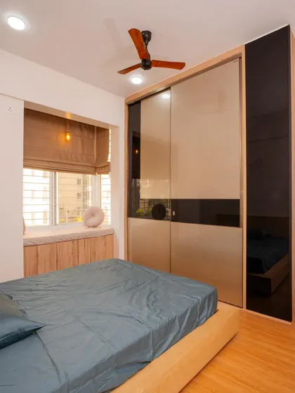 A modern minimalist bedroom at Mana Capitol, featuring a sleek sliding wardrobe with black glass accents and a cozy window seat for relaxation.