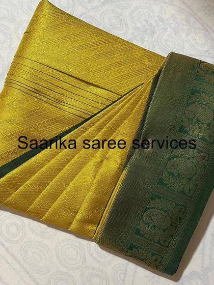 A beautiful yellow silk saree with a green border, showing the crisp pleats of my folding service.