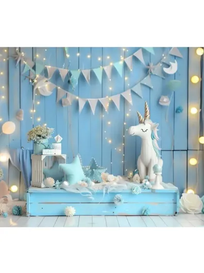 A magical unicorn-themed backdrop in shades of blue, complete with fairy lights, bunting, and a unicorn statue for a dreamy birthday setup.