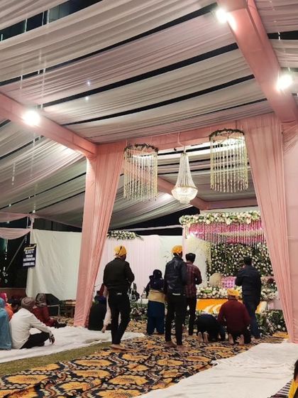 An indoor setup for an Anand Karaj ceremony. The simple pink and white decor with elegant chandeliers creates a peaceful and respectful environment.