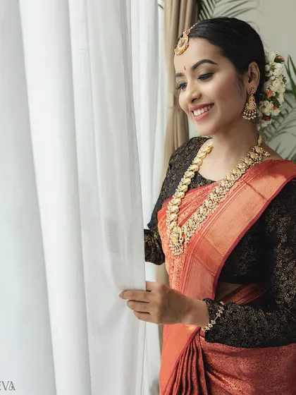 A candid-style portrait of a model in a rust-colored saree with a black lace blouse. Her joyful smile and the natural light from the window create a warm and inviting feel for this ethnic wear shoot.