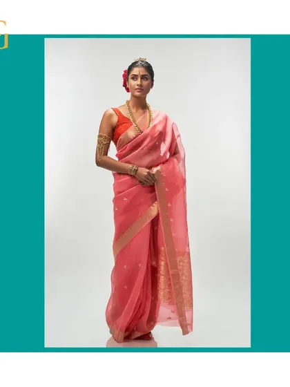 This ethereal salmon silk organza saree is adorned with delicate gold zari buttis. The pallu features an intricate floral motif, making it a piece of wearable art.