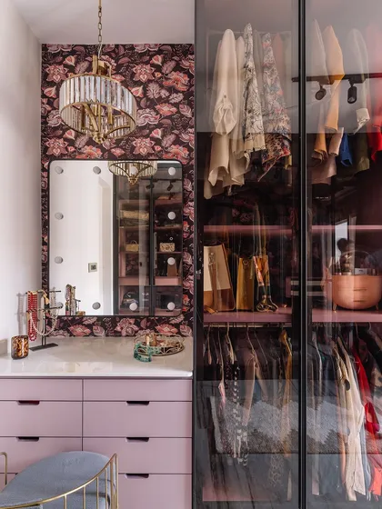 This chic walk-in closet is a dream come true, featuring custom lilac cabinetry, a vanity with Hollywood-style lighting, and glass-front wardrobes. We designed this space to be both a functional dressing room and a personal style sanctuary.