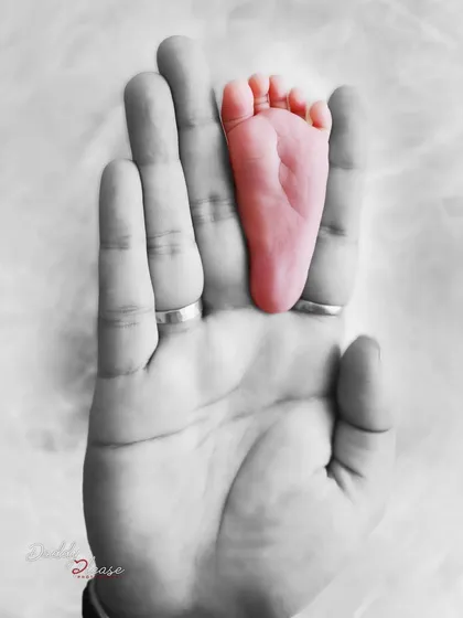 An artistic photo with selective color, highlighting the baby's pink foot against the black and white image of a parent's hand. This editing style creates a unique and memorable image.