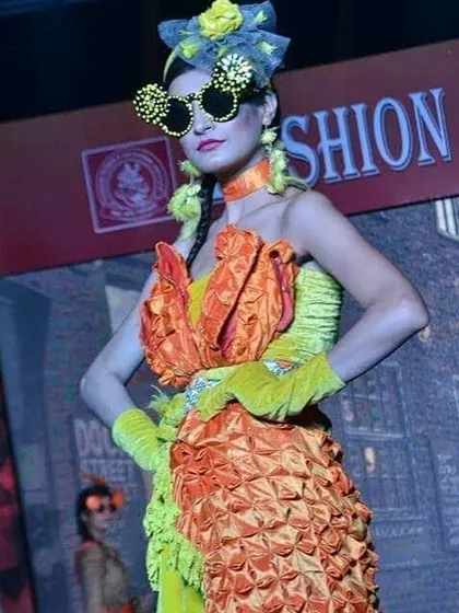 A close-up of a highly creative student design from a fashion show. This piece features complex fabric manipulation techniques on the bodice and skirt, paired with handmade accessories to create a unique, high-fashion look.