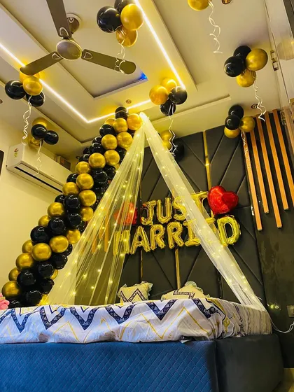 This angled view highlights the ceiling decor, with bunches of black and gold balloons hanging down. The warm glow from the fairy lights and the illuminated ceiling creates a cozy and celebratory atmosphere.