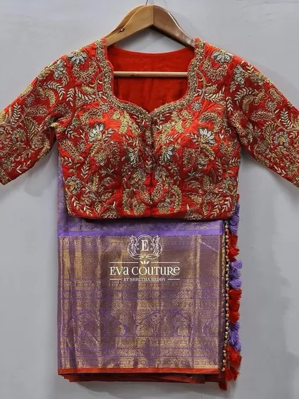 A heavily embroidered blouse and saree set. The red blouse is covered in dense gold zardozi work, designed to be paired with the lilac Kanchi pattu saree.