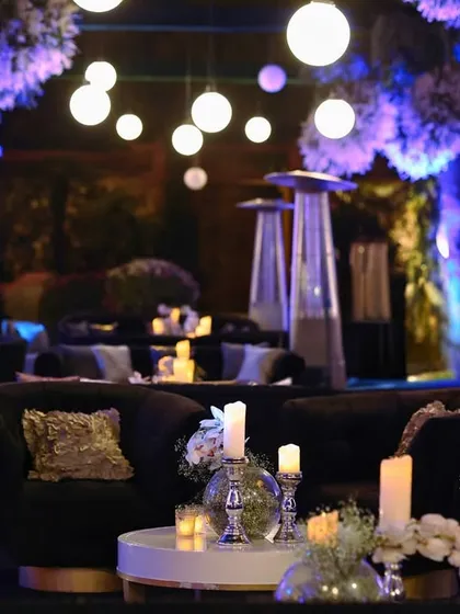 An elegant lounge setting with deep blue velvet sofas, where the tables are adorned with simple glass vases of baby's breath and glowing candles.