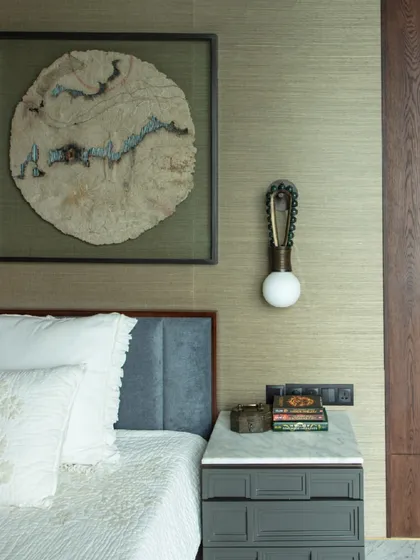 A bedroom in 'The 42, Kolkata', featuring unique wall art made from tree bark. The custom bedside table and chain-link light fixture add an industrial-chic touch to the serene space.